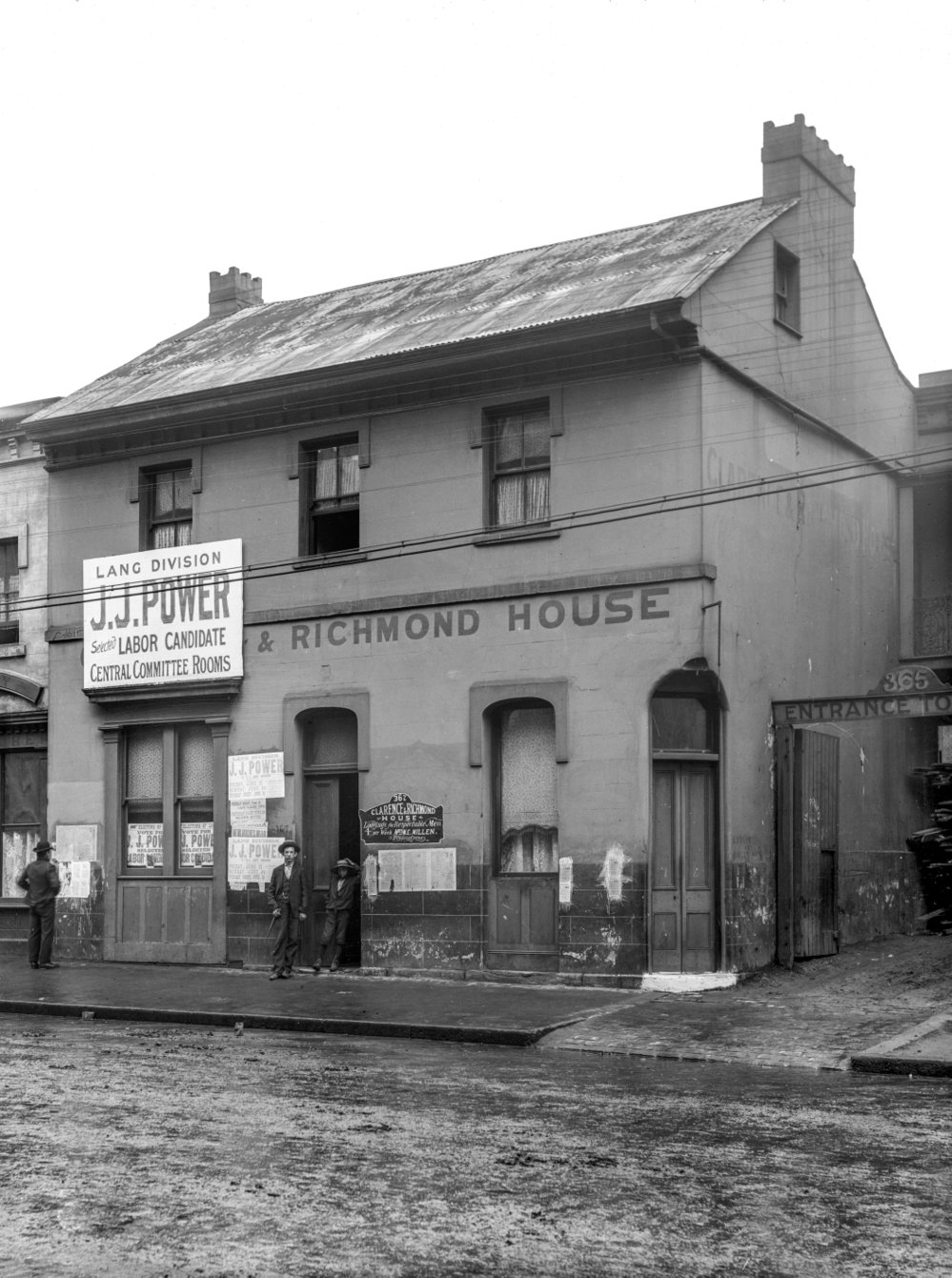 The two-storey former Clarence and Richmond Hotel at 367 Kent Street, Sydney, photographed circa 1901, by then a boarding house called Clarence and Richmond House, its façade pasted with election posters for the 1901 state election and three men standing on the pavement outside.