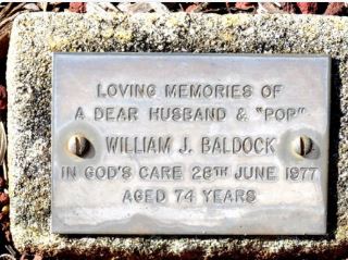 A small bronze memorial plaque reading "Loving memories of a dear husband & Pop, William J. Baldock, in God's care 28th June 1977, aged 74 years."