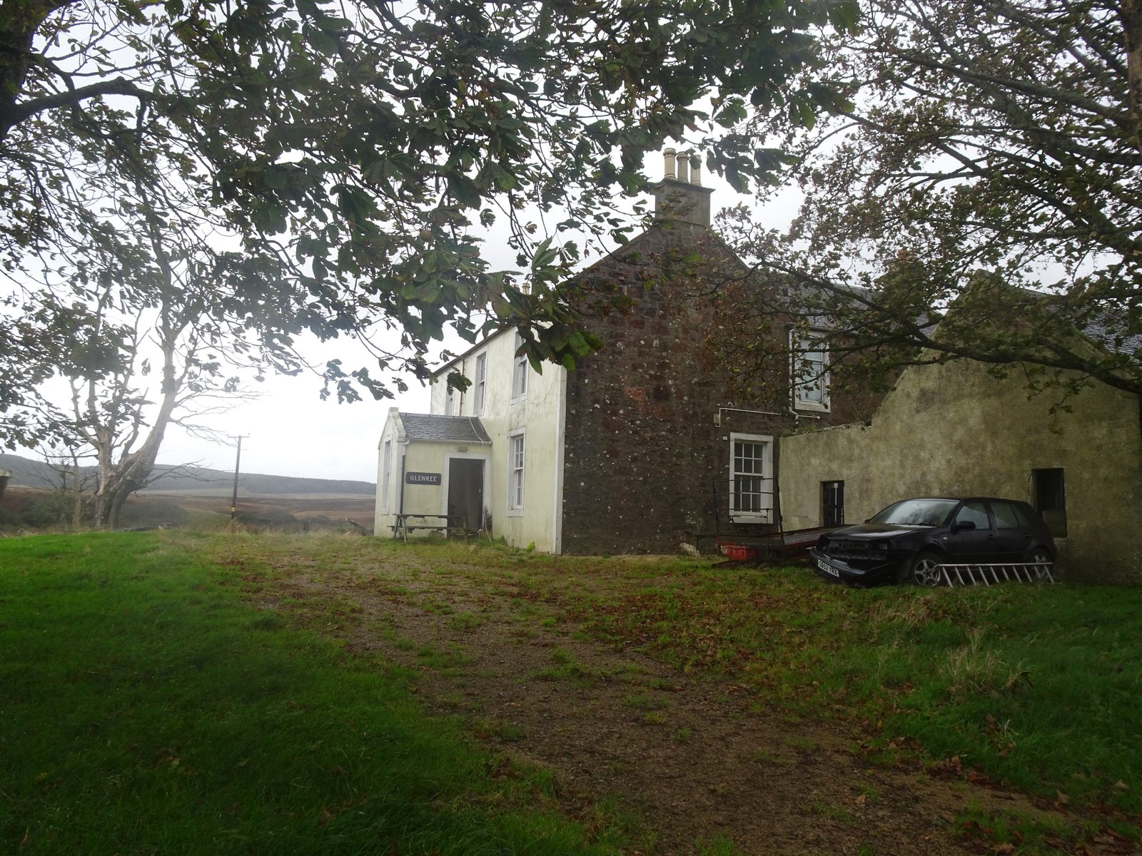A whitewashed two-storey farmhouse with a stone gable and a small porch bearing the name board Glenree, seen under trees, with moorland beyond.