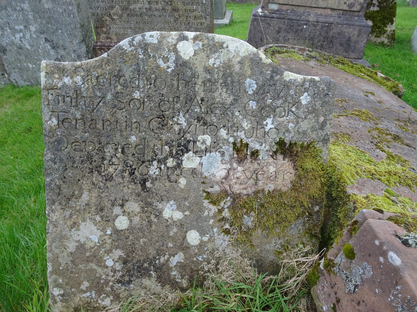A weathered eighteenth-century headstone covered in lichen and moss, its italic lettering reading: Sacred to the Memory of Finlay, Son of Alex. Cook, Tenant in Claynod, who departed this Life 178–, aged 21 years.