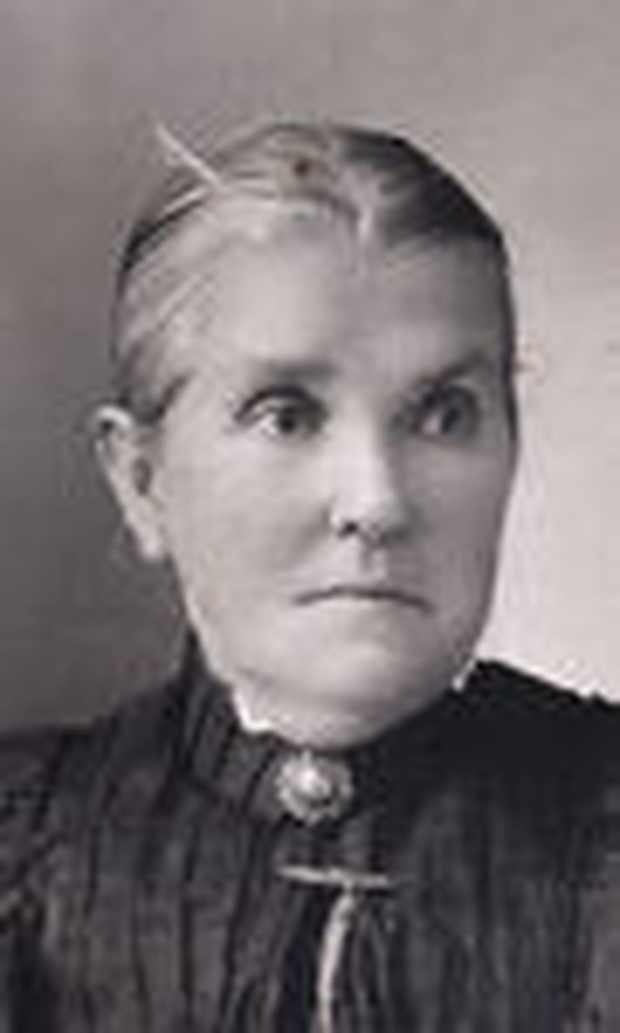 Head-and-shoulders photograph of an elderly woman with hair drawn back, in a dark high-necked dress with a brooch at the throat.