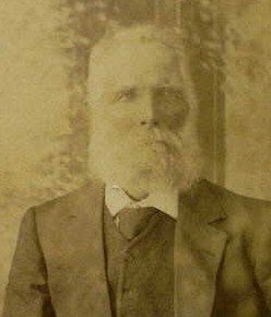 Faded studio portrait of an elderly man with a full white beard and moustache, in a dark suit and tie.