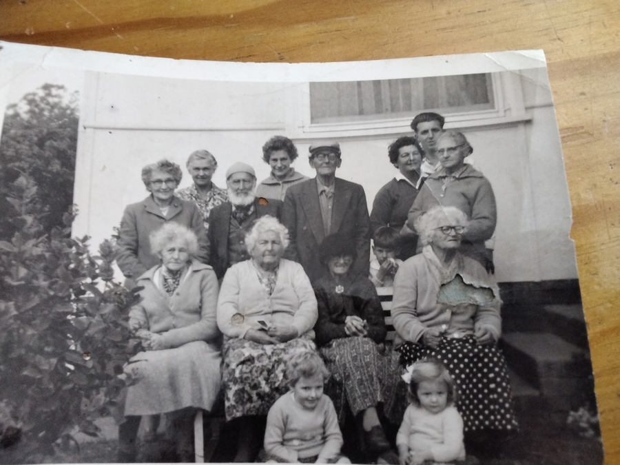 Black and white snapshot of a family group in a garden — six older adults standing, four older women seated in front, with a younger couple, a boy and two small children.