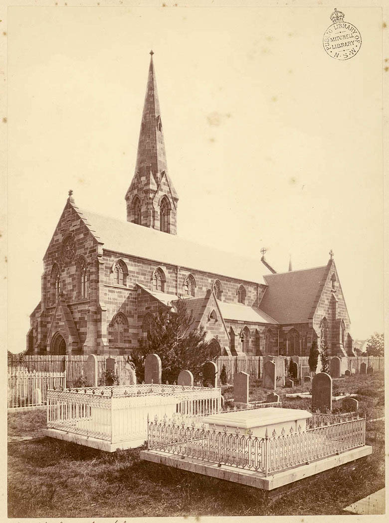 Sepia photograph of St Stephen’s Church, Newtown, a Gothic Revival sandstone church with a tall spire, photographed around 1875 in its churchyard, its iron-railed graves still new and its trees not yet grown.
