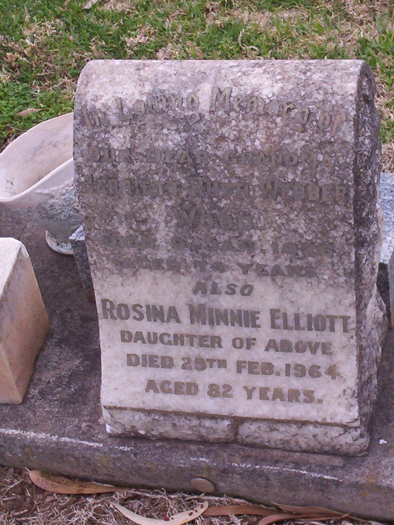 A small gabled headstone of weathered pale stone in a lawn cemetery, the lettering worn but legible: in loving memory of a grandmother, Harriett Ruth Webber Wood, and below her a daughter, Rosina Minnie Elliott.
